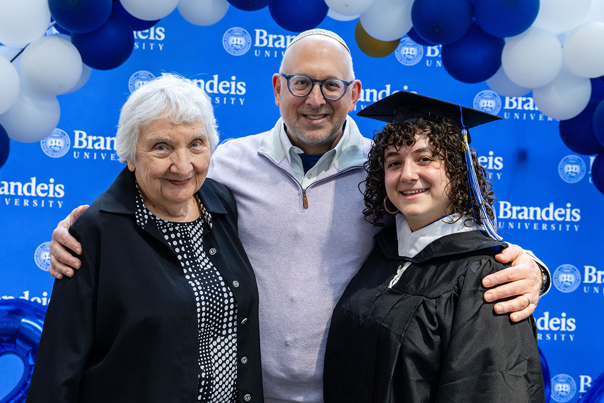 Joy Fish ’56, Ron Fish ’91 and Nili Fish-Bieler ’26 stand in front of a Brandeis banner