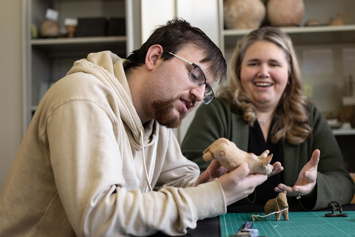 A student sits at a table with a professor and examines an ancient artifact.