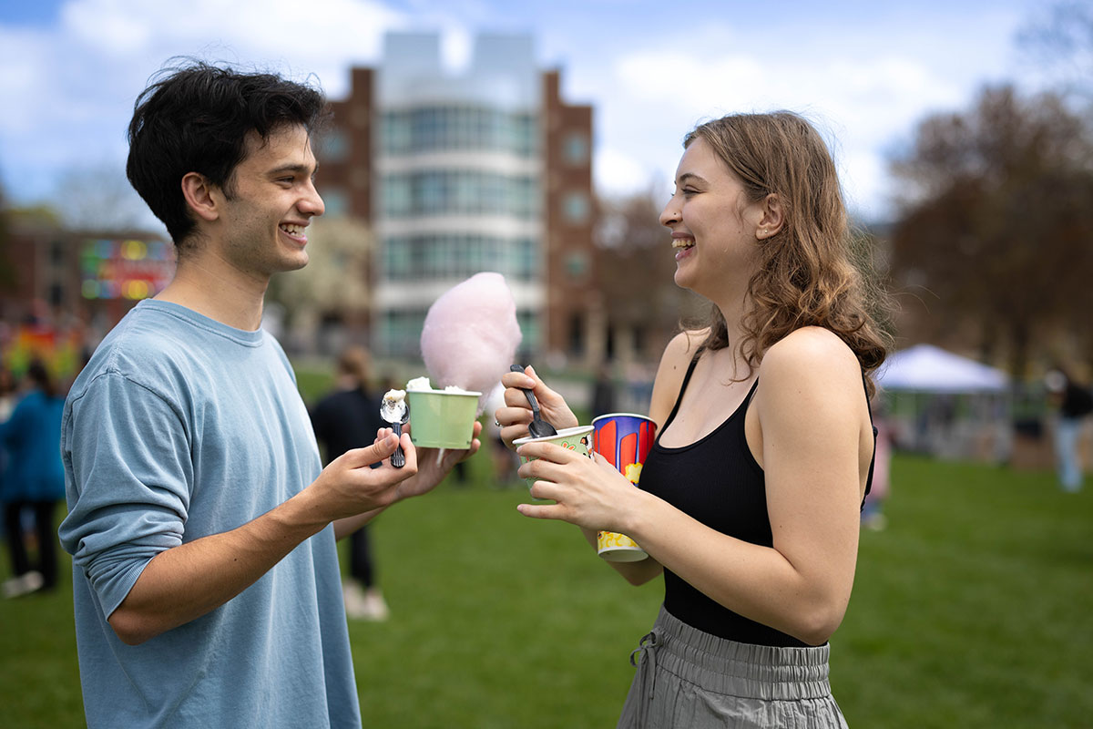 Two students laugh together while eating cotton candy and ice cream.