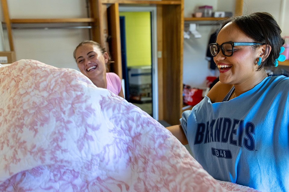 Two students make a bed in a dorm room.