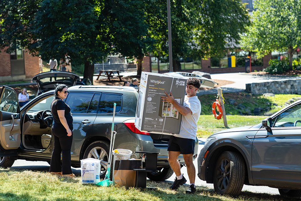 A student lifts a large box on move-in day.