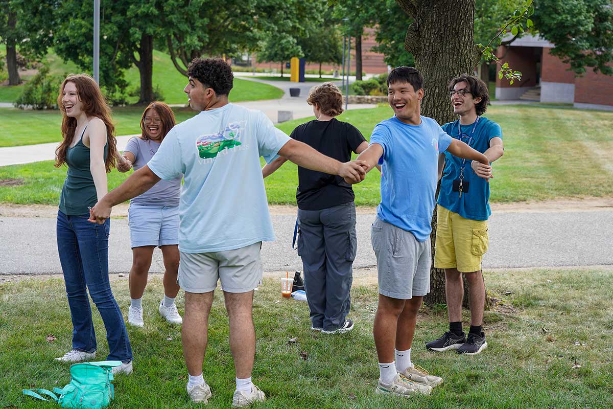 A group of undergraduate students stand outside on campus holding hands during a group activity.