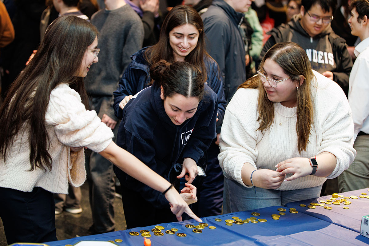 Three students stand at a table with Hanukkah gelt.