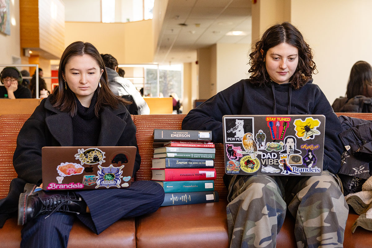 Two students sit in the library and study on their laptops.