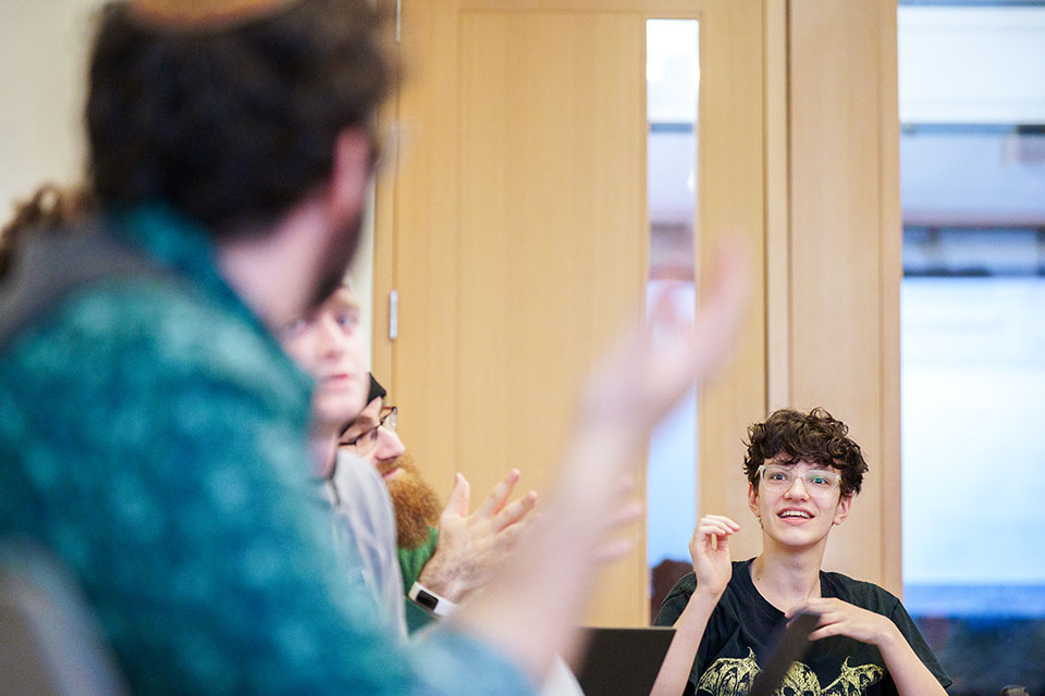 Two students sitting in a classroom talk with eachother.