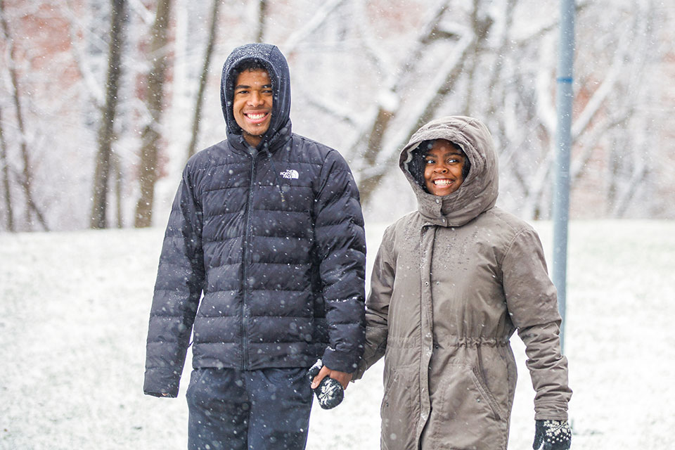 Two students walk on a snow-covered campus while holding hands.