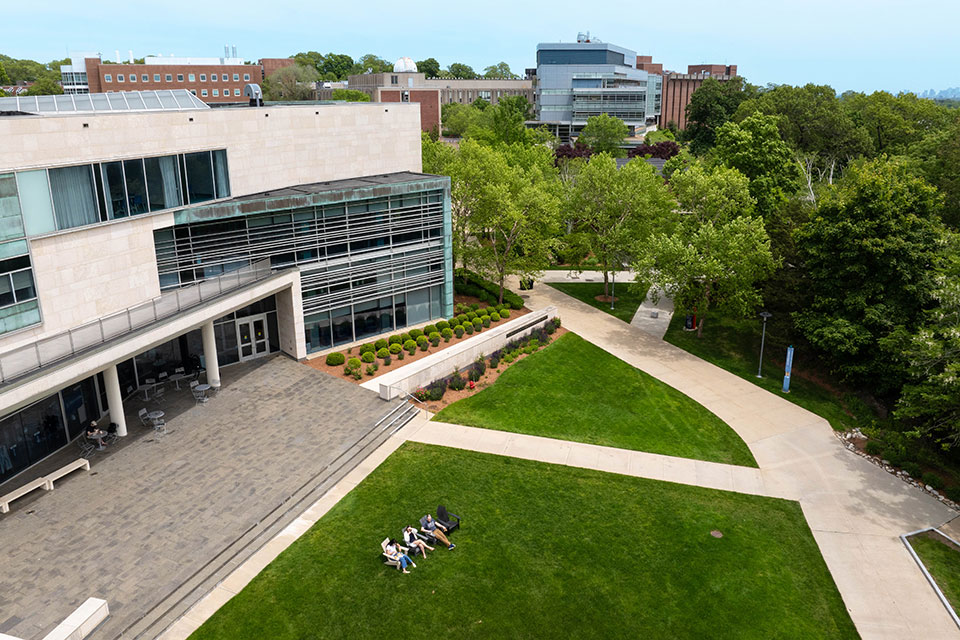 An aerial view of the Brandeis campus with three students sitting together outside.