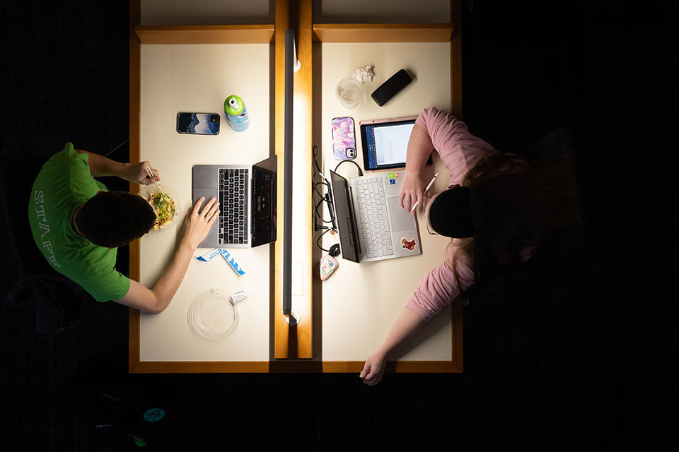 An aerial view of two students studying on their laptops in the library.