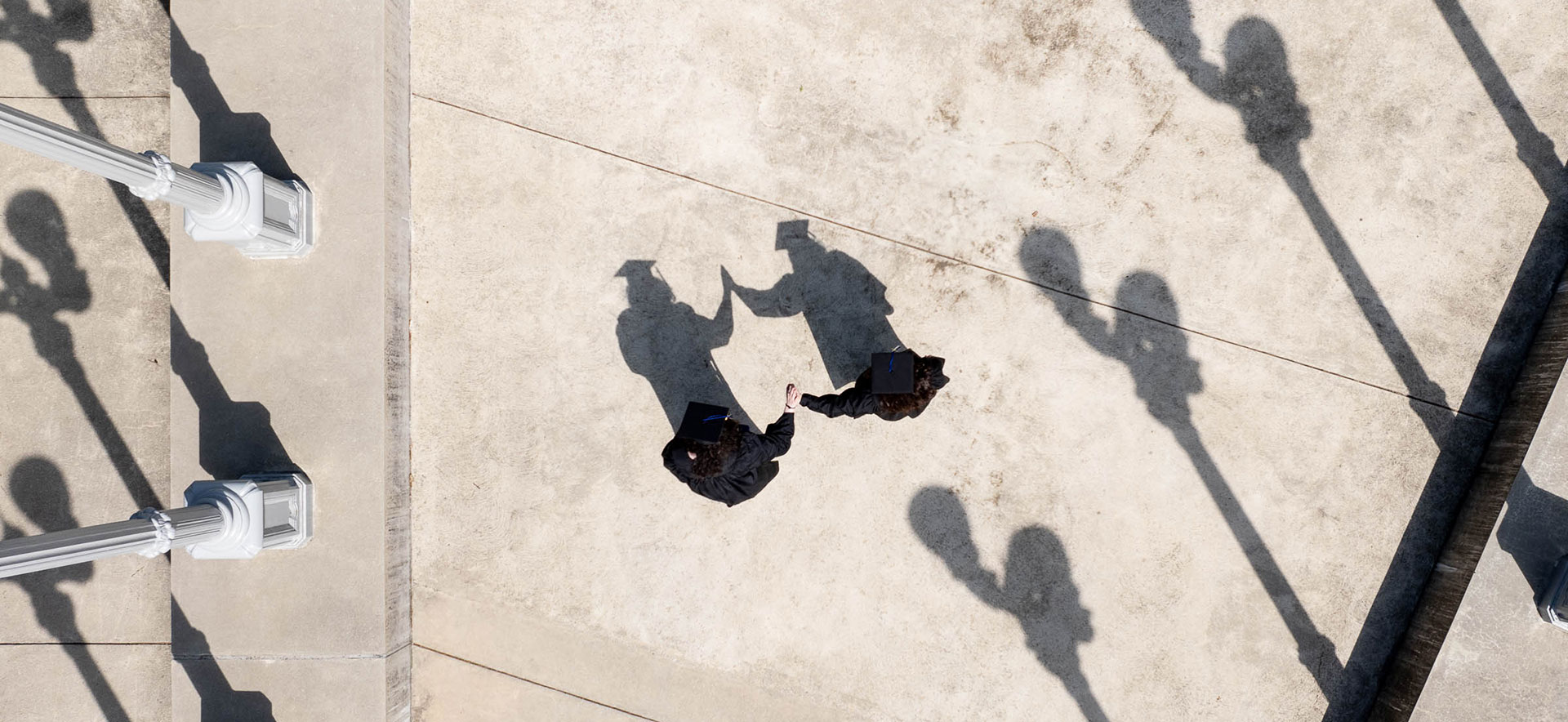 An aerial view of two students dressed in academic regalia high-fiving at "The Light of Reason" sculpture ahead of Commencement.