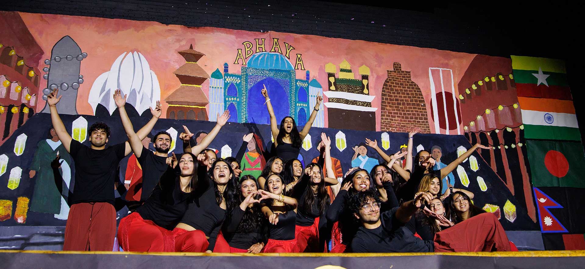 A group of students pose on stage in front of a colorful backdrop.