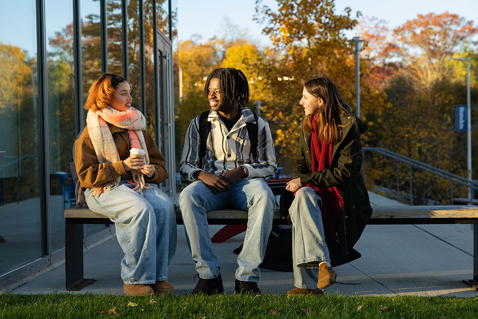Three students sit on a bench outside on campus.