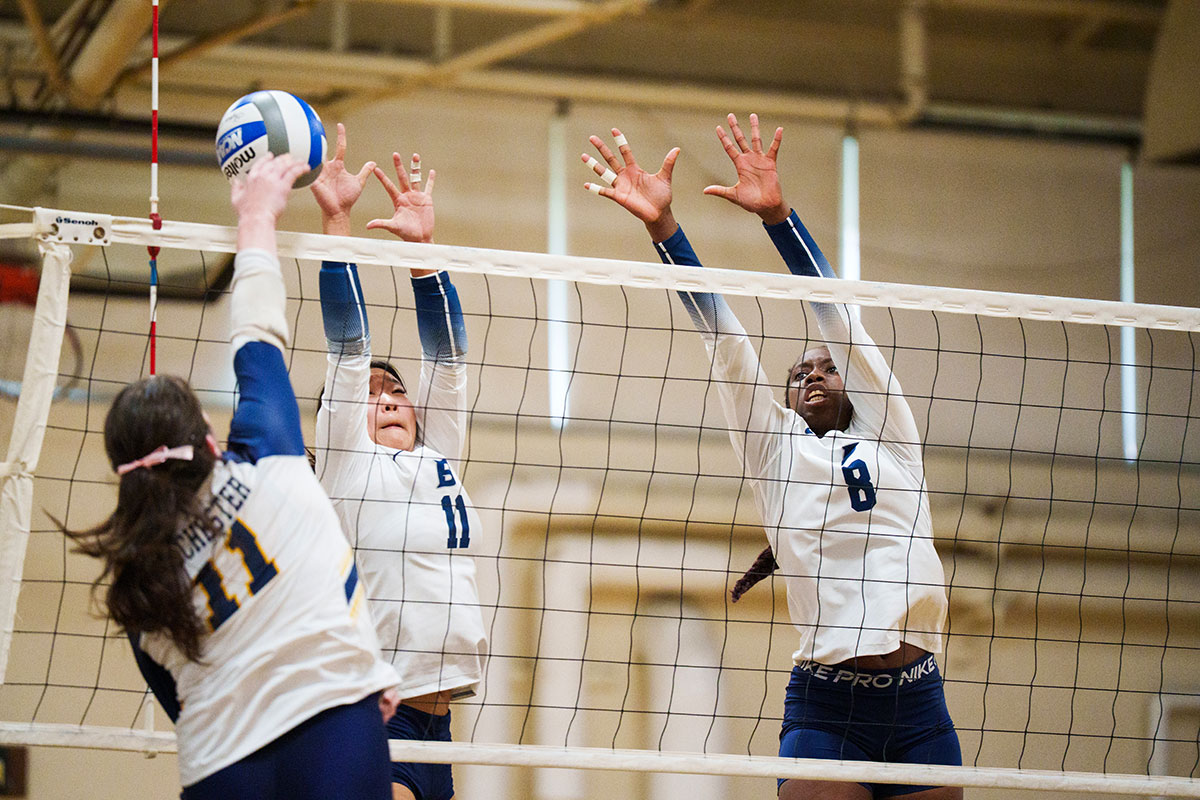 Three women play indoor volleyball.