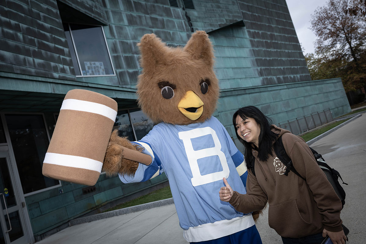 A student poses with the Ollie the Owl mascot.