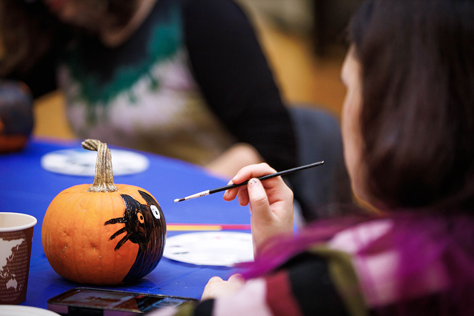 A person paints a black cat on a pumpkin.