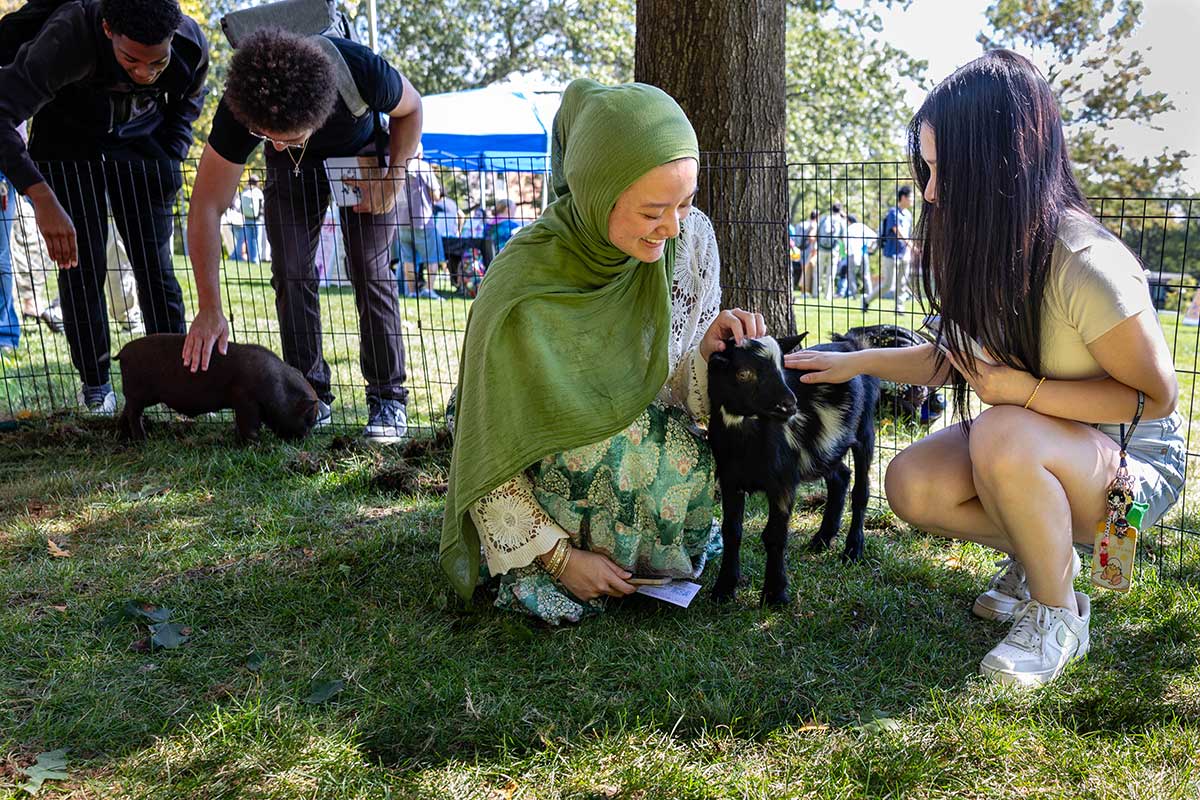 Two students pet a baby goat.