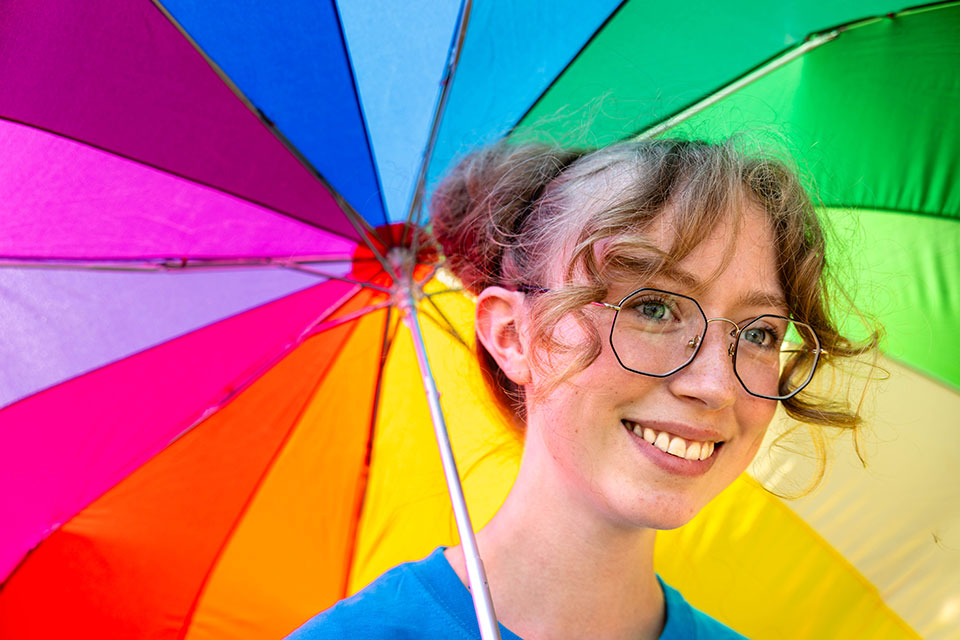 Jessy P. stands under a colorful umbrella.