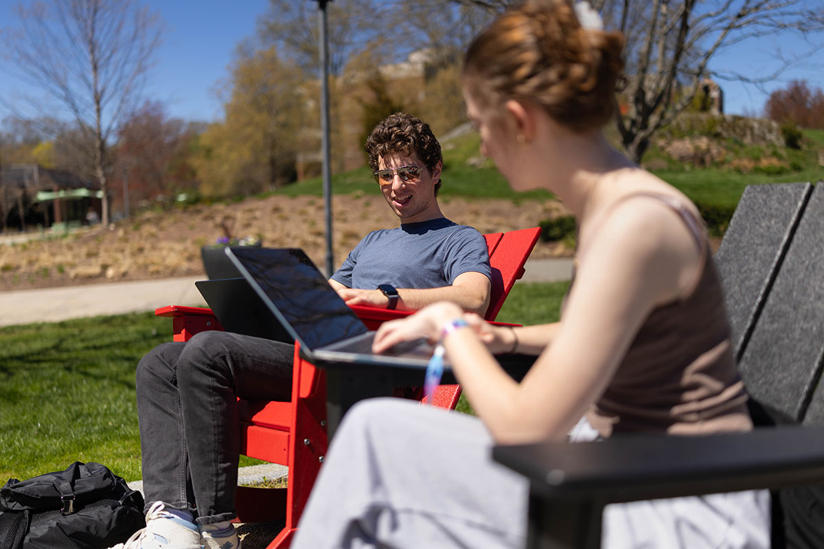 Students study on their laptops outside during a sunny day on campus.