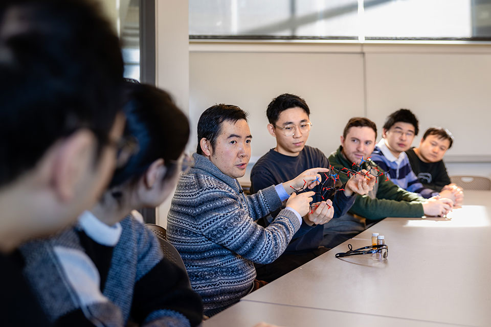 A professor explains a carbohydrate model with students sitting at a table.