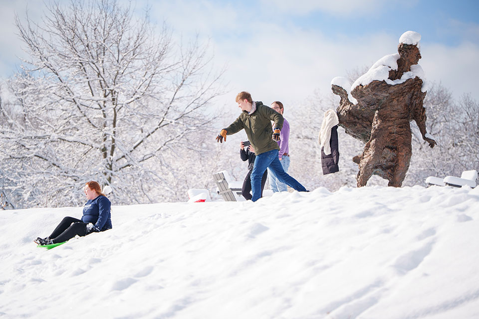 Students sled and have a snowball fight by the Louis Brandeis statue on campus.