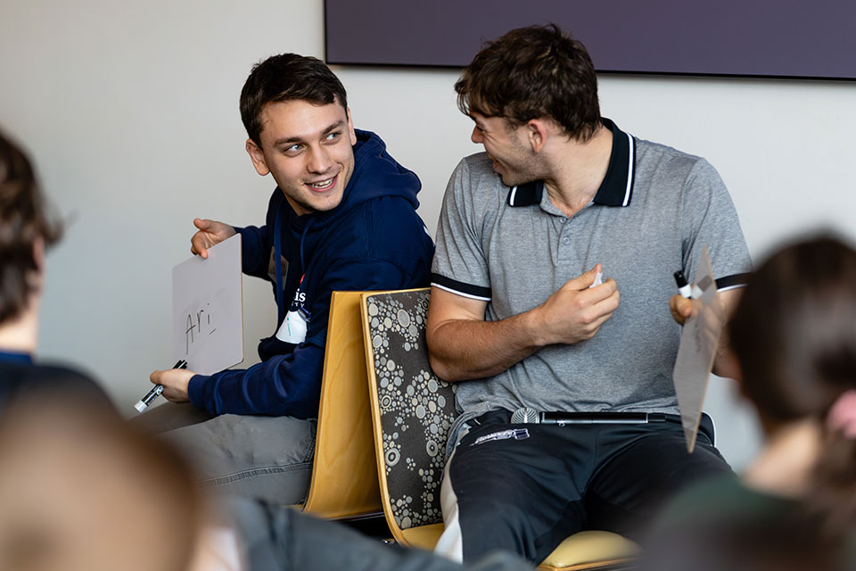 Prospective students sit back-to-back in chairs as part of a game during Inside Deis Day.
