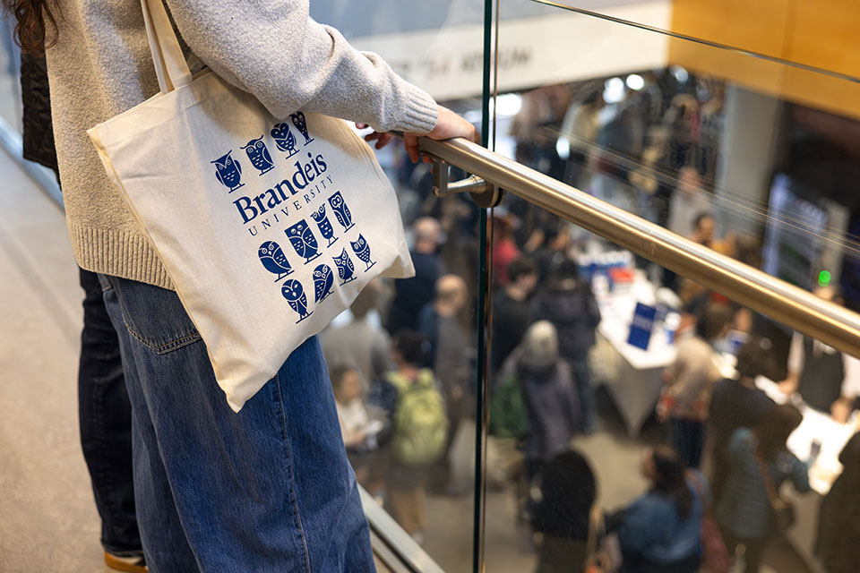 A student stands with a Brandeis University tote bag.