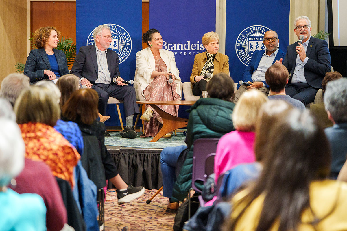 A panel of speakers speak together on stage as an audience looks on.