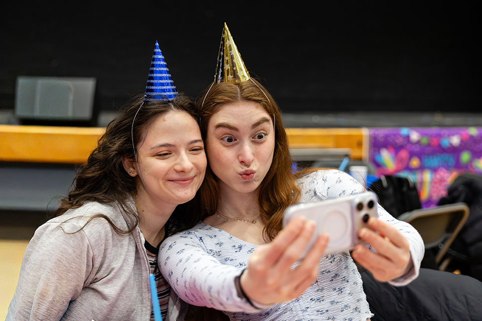 Two students wearing party hats take a selfie.