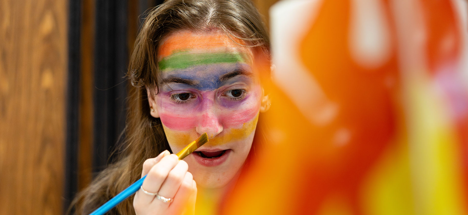 A student paints a rainbow on their face.