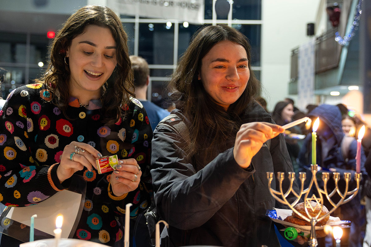 Two students smiling while lighting a menorah