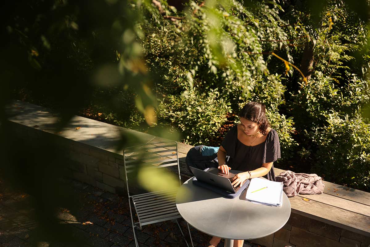 Person seated outdoors at a table using a laptop