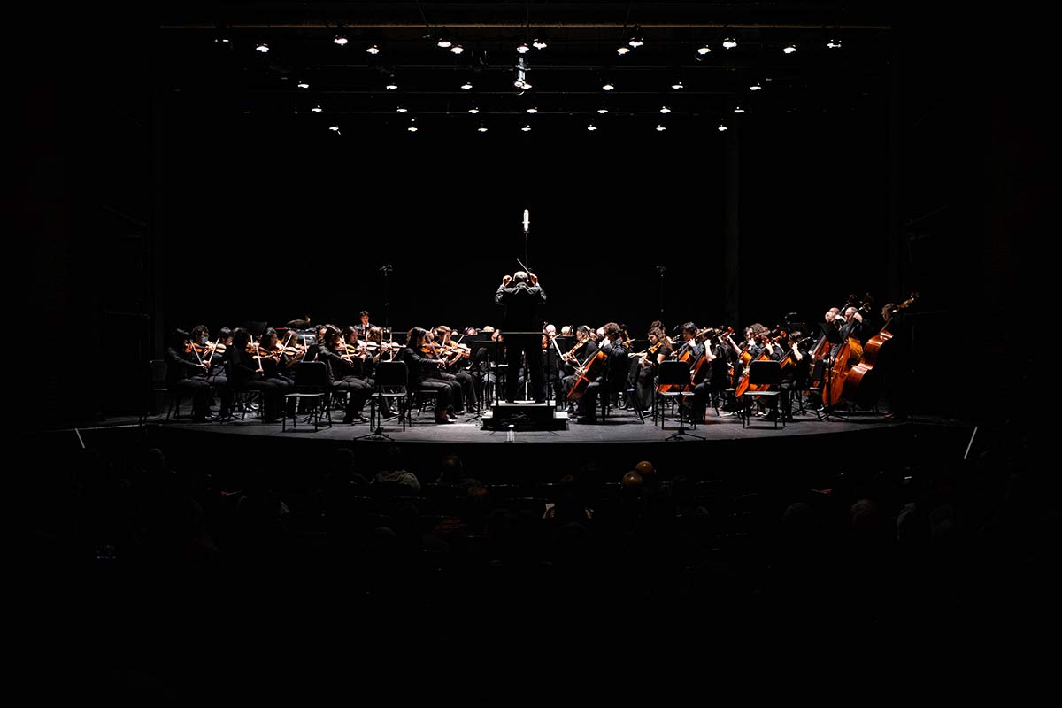 An orchestra plays on stage, while the rest of the photo is dark.