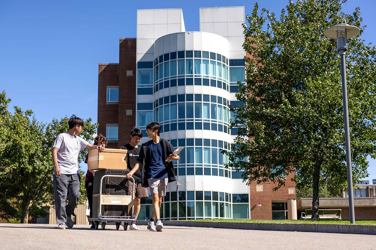 People walking on campus towing a cart, the Volen building is seen in the background