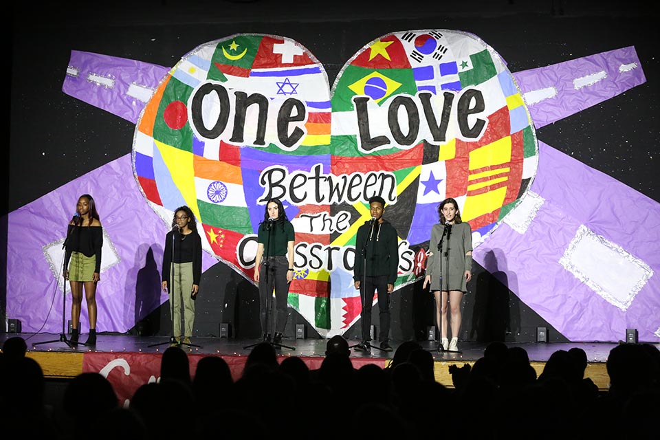 Students on stage in front of a banner that reads One Love Between the Crossroads