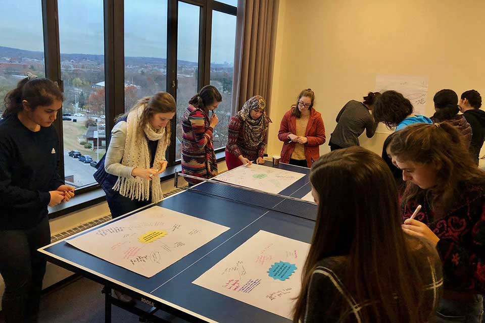 Women stand around a table, looking at poster boards