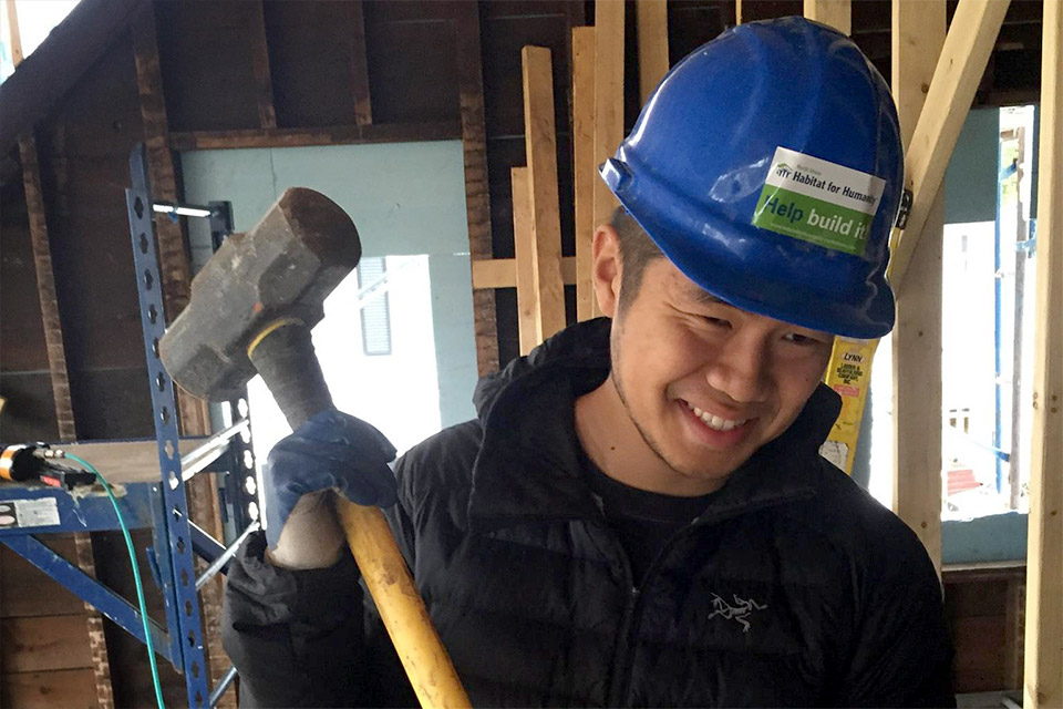 A student wearing a hard hat and carrying a sledgehammer