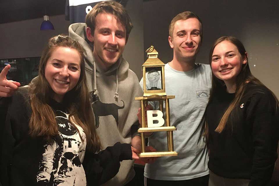 Four students smile while holding the Trivia Night trophy