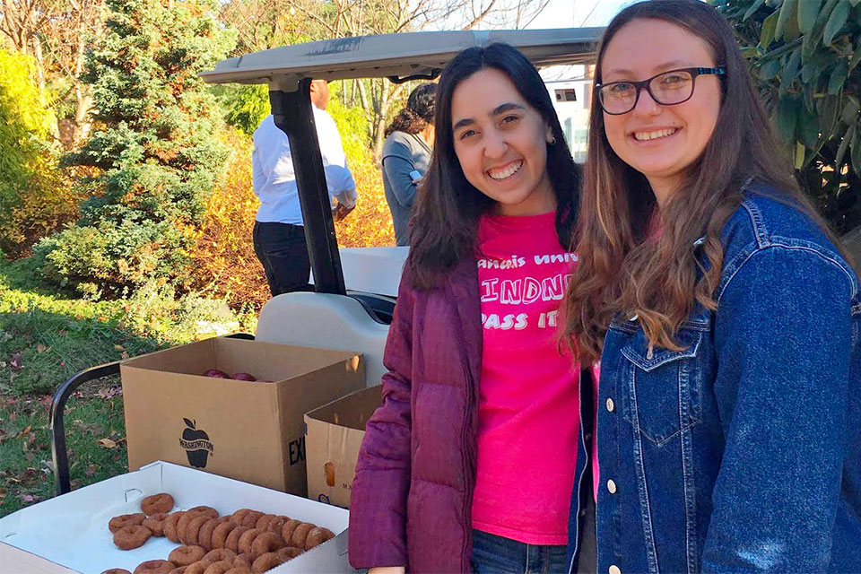 Two students smile standing in an apple orchard