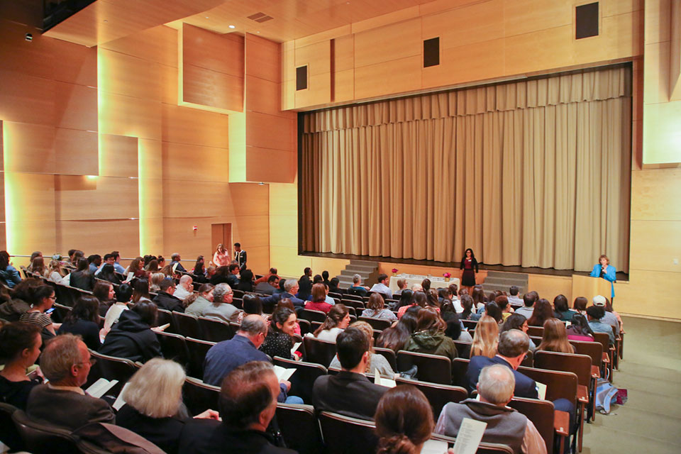 People sit in the Shapiro Theater. The curtains are closed