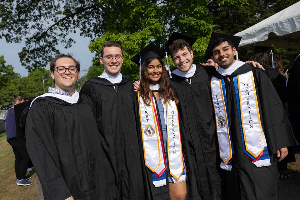 Students smiling wearing caps and gowns outside the Brandeis Commencement ceremony.
