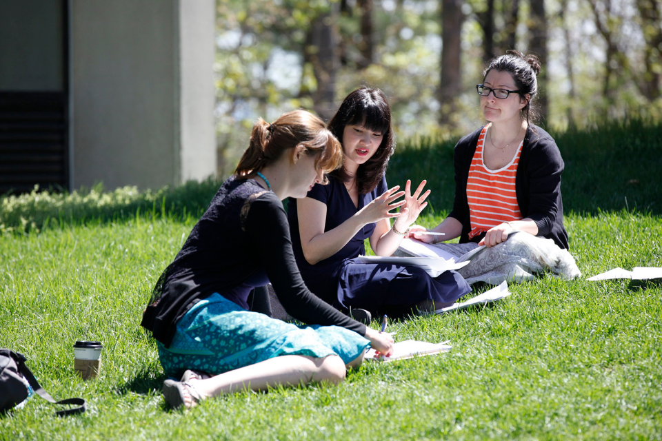 Three students discuss their coursework outside.