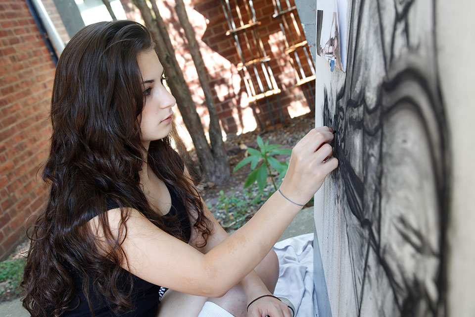 Student creating a work of art using charcoal