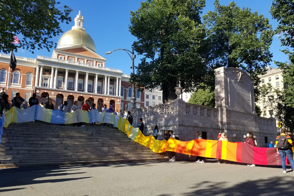 students holding warming stripes banner in front of MA statehouse