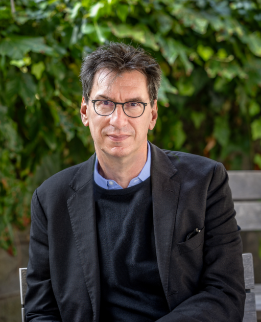 Photo of Peter Gordon sitting on a bench in front of green foliage in the background
