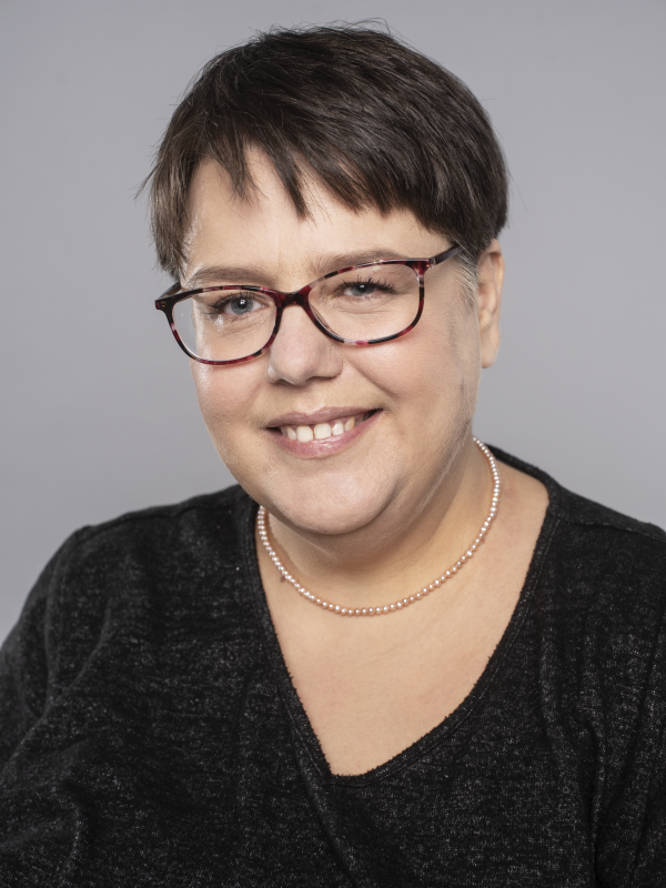 A headshot of Ildikó Barna with brown framed glasses looking into the camera and smiling.