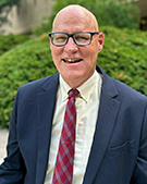 The portrait photo of Thomas Burman wearing a suit and glasses with a green environment.