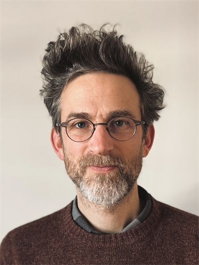 headshot of Tomaz Jardim wearing glasses and a dark red sweater