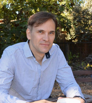 A portrait photo Sven-Erik Rose wearing a bright blue shirt with the leafy green background