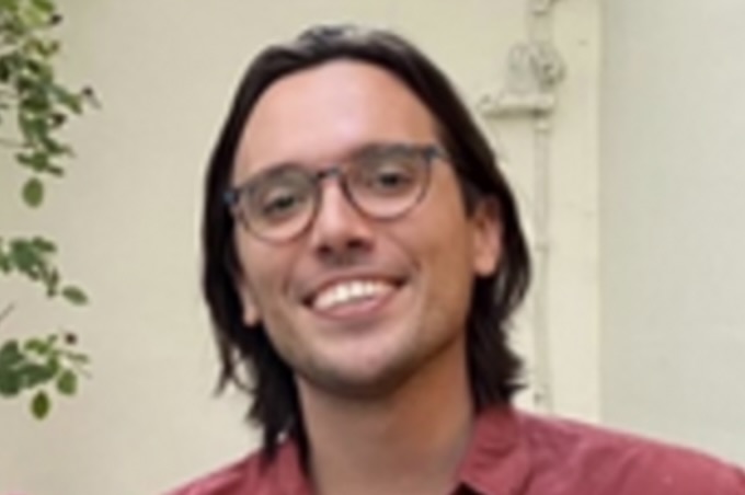 Portrait photo of Trevor Wilson, wearing a burgundy shirt and glasses