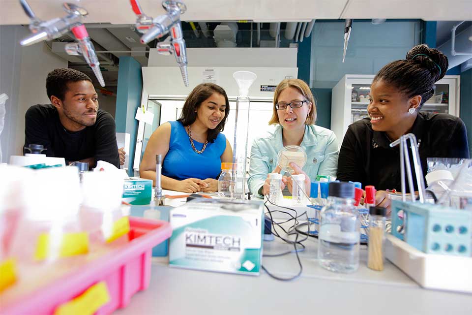 Three student sit with a professor in a science lab