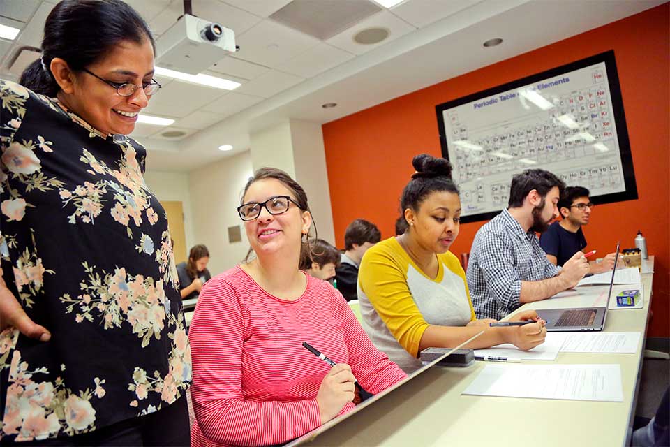 A professor stands next to a sitting student during class